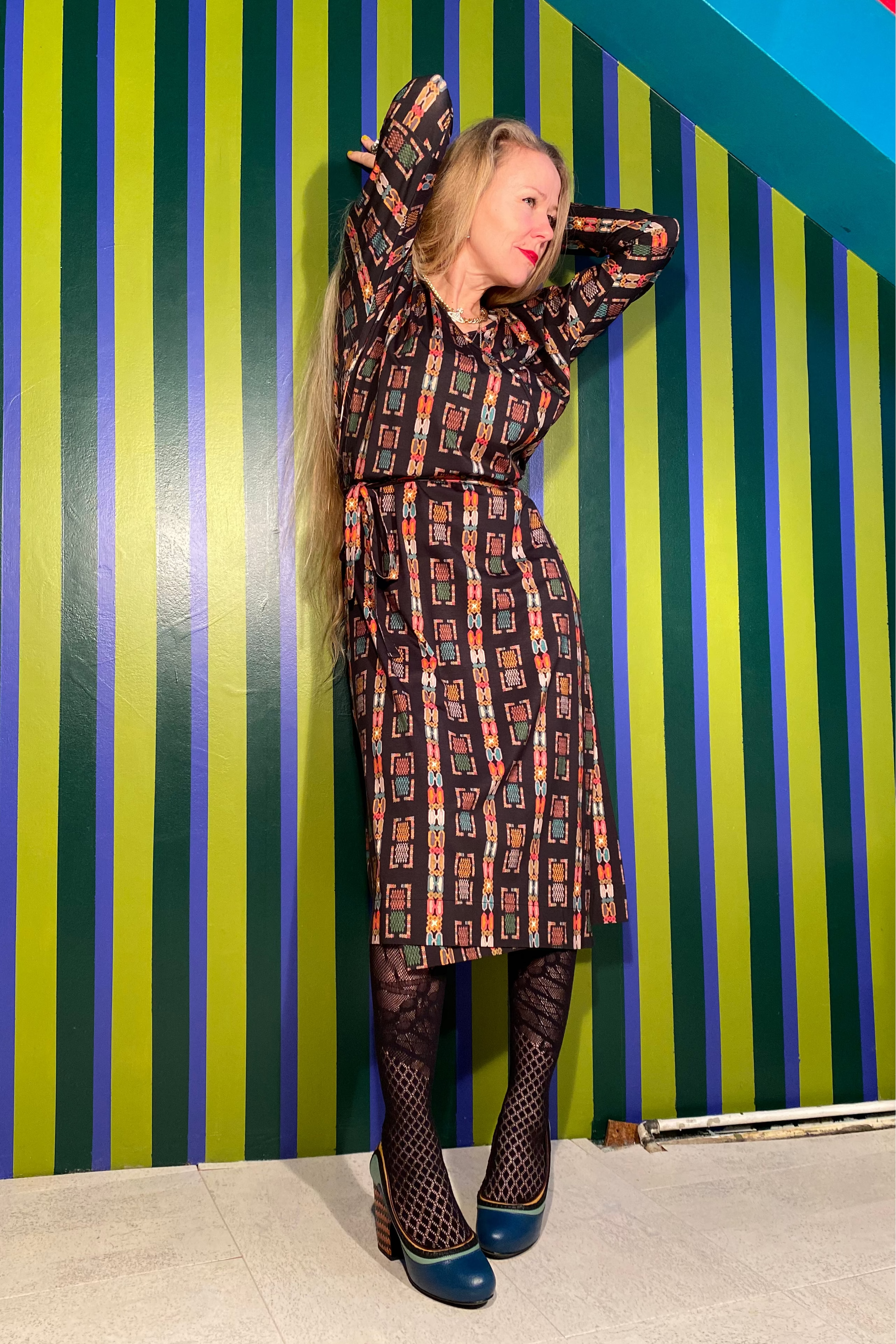 Person wearing a patterned dress against a striped wall.