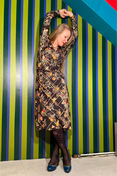 Person wearing a long floral coat against a striped wall.