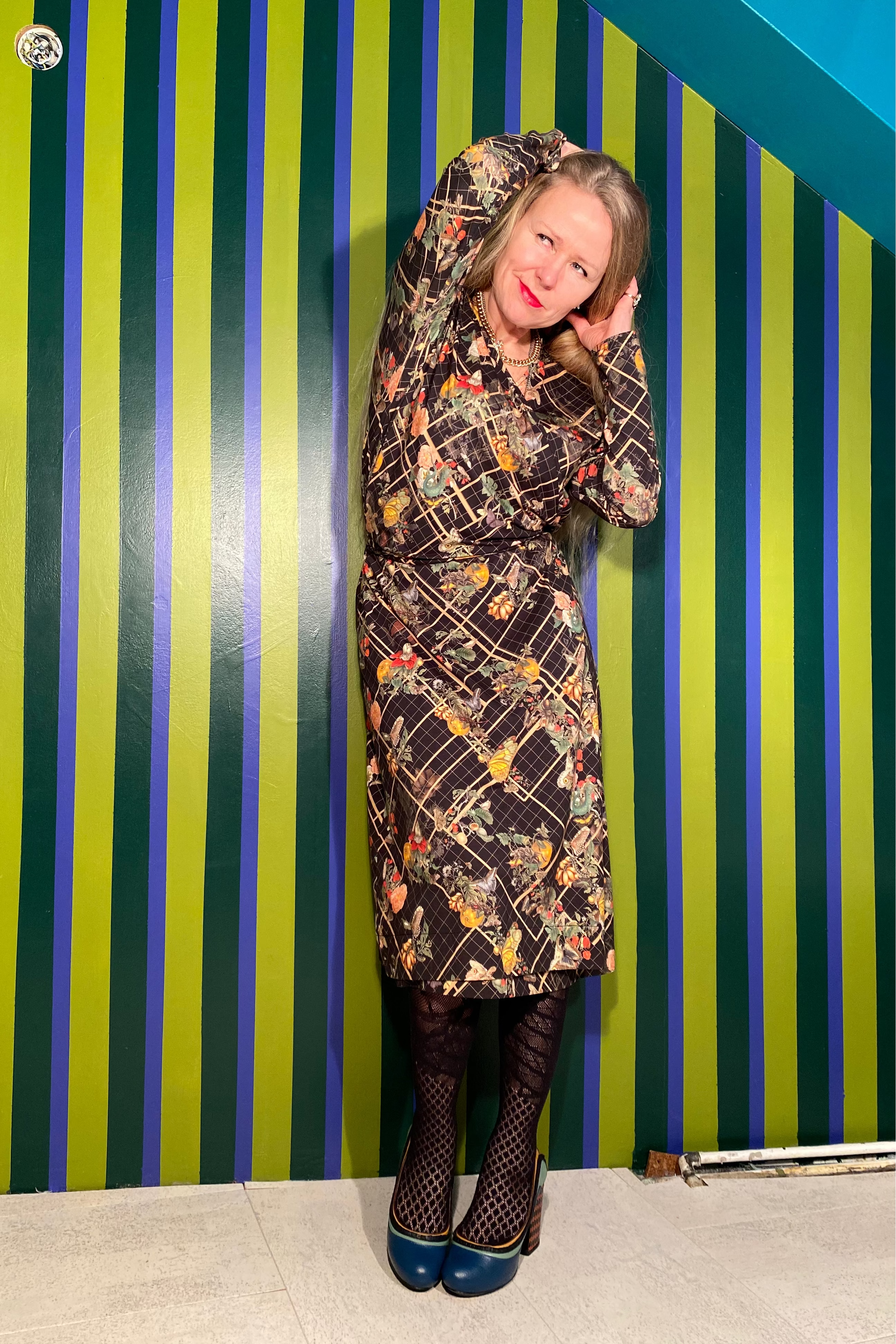 Person wearing a patterned coat against a striped green and blue wall.
