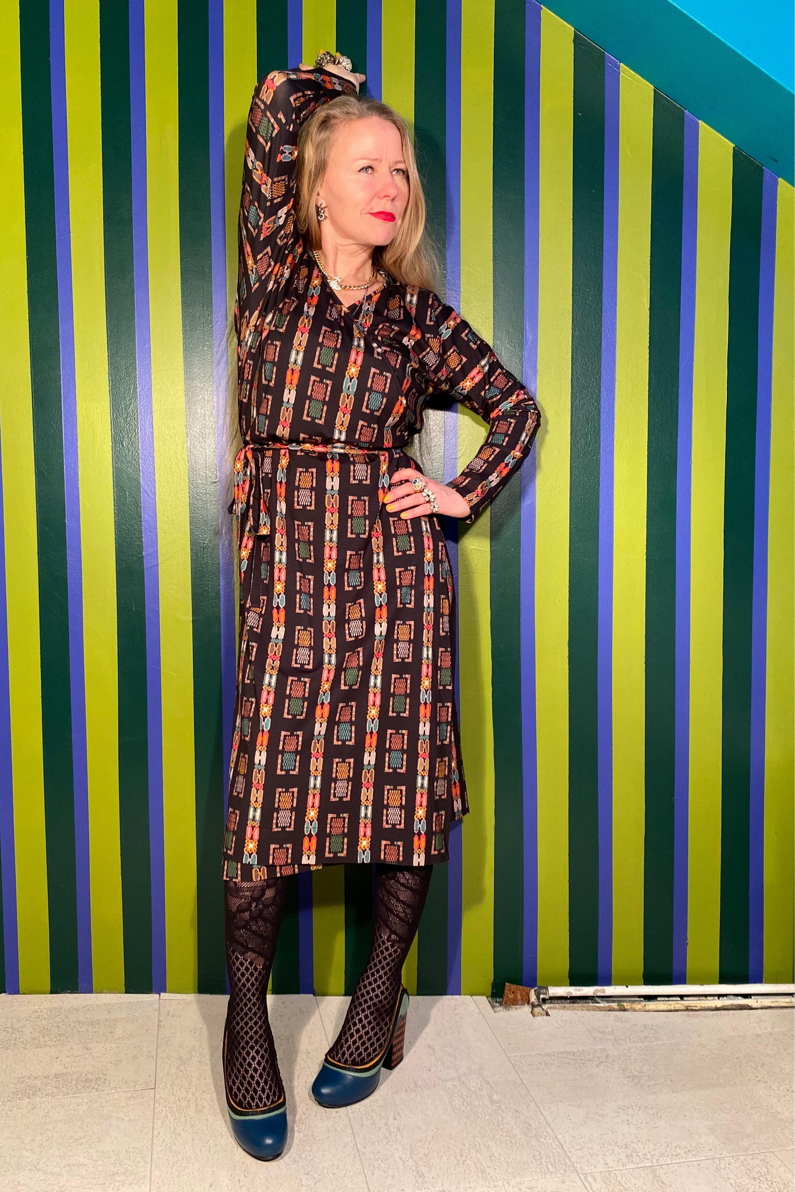 Woman in a patterned dress posing against a striped wall.