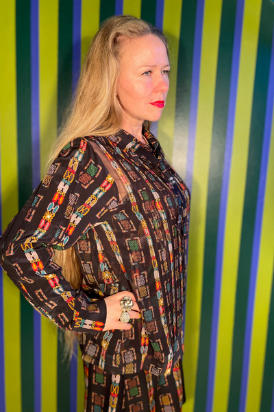 Woman wearing a patterned outfit standing against a striped green and blue background